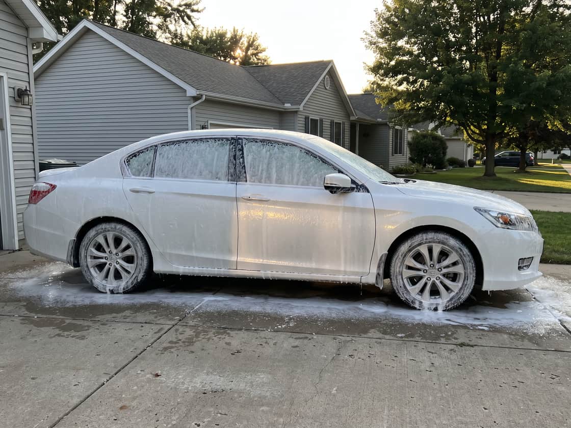 Car under an even blanket of snow foam in a residential driveway